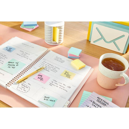 En åben planlægger viser en ugeplan på et skrivebord, omgivet af håndskrevne noter, en pen, kontorartikler, små kort, en kop te og Post-it® genbrugssedler (38 mm x 51 mm) fra 3M Deutschland GmbH.