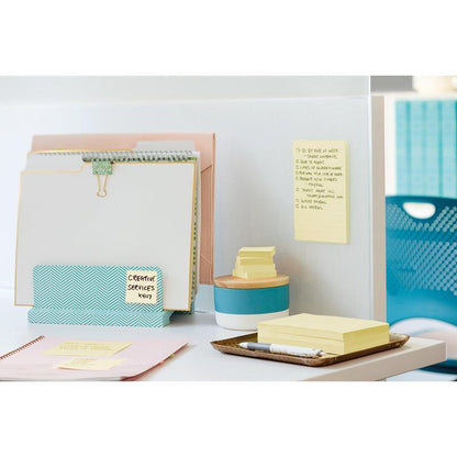 På et hvidt skrivebord er der 3M Post-it® Super Sticky Notes (76 mm x 127 mm, 90 ark/blok, 100% PEFC) fra 3M Deutschland GmbH, som er fastgjort på en skillevæg og stablet ved siden af en blå beholder, ved siden af ringbind og kontorartikler.