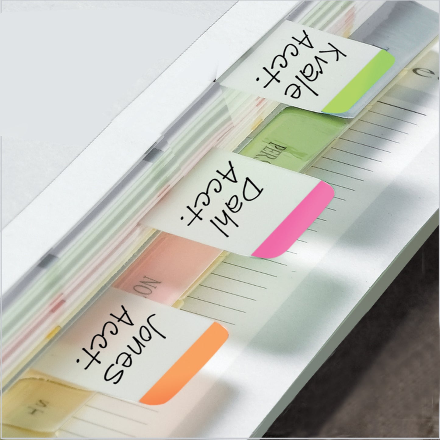 Eine Nahaufnahme eines Aktenordners, der mit Post-it® Index Strong Ablagetabs der 3M Deutschland GmbH organisiert ist. Farbige Tabs in Orange ("Jones Acct."), Rosa ("Dahl Acct.") und Grün ("Kale Acct.") markieren verschiedene Dokumentenabschnitte.