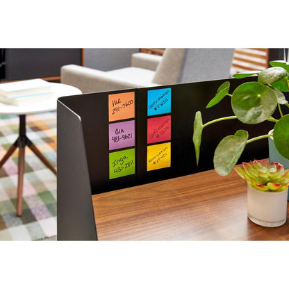En nærbillede af en skrivebordsopdeling med seks farverige Post-it® Super Sticky Notes (76 mm x 76 mm, 90 ark/blok, 100% PEFC) fra 3M Deutschland GmbH, der viser detaljer. En grøn plante og uskarpe kontormøbler fuldender scenen.