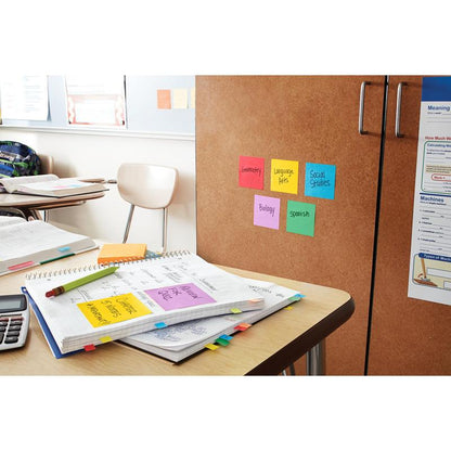 På skrivebordet i et klasseværelse ligger åbne hæfter, papirer, en lommeregner og Post-it® Super Sticky Notes (76 x 127 mm, 90 ark/blok, 100% PEFC) fra 3M Deutschland GmbH. På et skab i nærheden er der farverige sedler med fagbetegnelser.