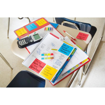 Et elevskrivebord med notesbøger, håndskrevne noter, en lommeregner, penne, markører, en mappe, mapper, papirer og Post-it® Super Sticky Notes (76 mm x 127 mm, 90 ark/blok) fra 3M Deutschland GmbH med tomme stole og flisegulv i baggrunden.