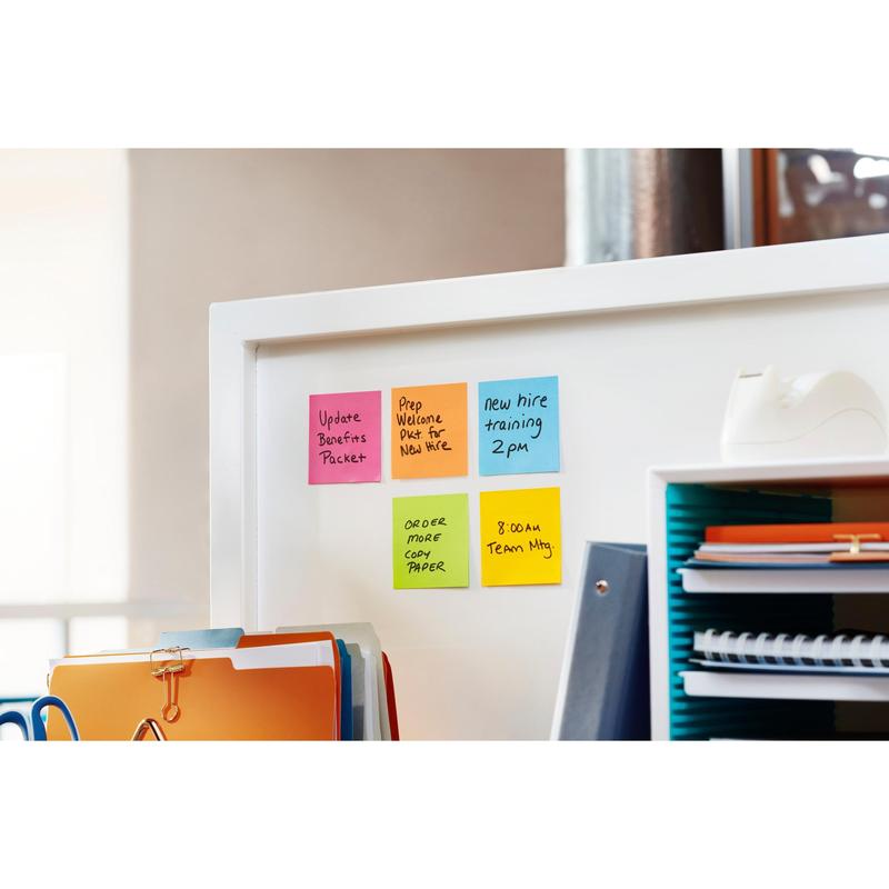 Et whiteboard med Post-it® Super Sticky Z-Notes (Blå, 76x76 mm) fra 3M og en hvid Post-it® Z-Notes dispenser i bjørneform står mellem kontorartikler som bunke af mapper, ringbind og en tapeholder på en arbejdsplads.